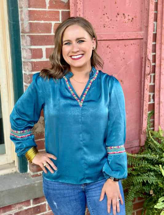 The Amy Top by Washco Apparel is an elegant teal shimmery fabric with colorful embroidery design around the v-notch ruffled neckline and sleeves.This top is long sleeve with an elastic band gathering around the wrist area, it can be pushed up or worn regularly.
