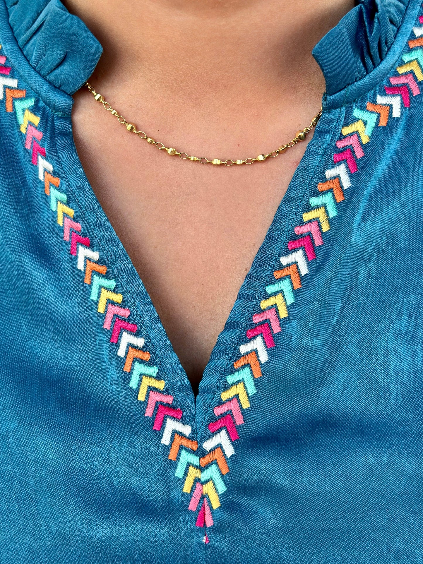 The Amy Top by Washco Apparel is an elegant teal shimmery fabric with colorful embroidery design around the v-notch ruffled neckline and sleeves. This top is long sleeve with an elastic band gathering around the wrist area, it can be pushed up or worn regularly.