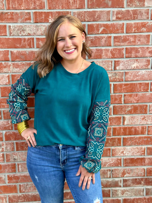 Stay warm, cozy and cute in the Cayce top by Washco Apparel! The Cayce top includes a soft sweatshirt fabric with colorful embroidered sleeves.