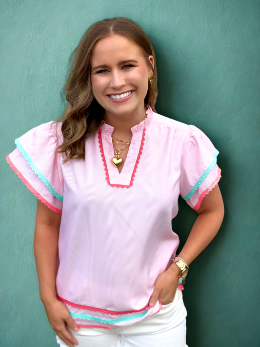 Woman wearing a pink blouse with colorful trim against a teal background