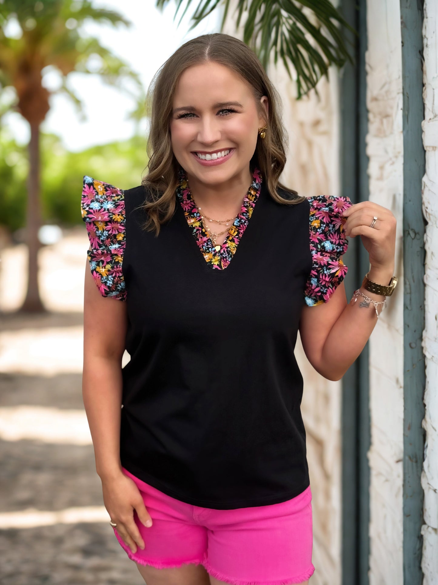 Woman wearing a black top with colorful sleeves and pink shorts, standing outdoors.