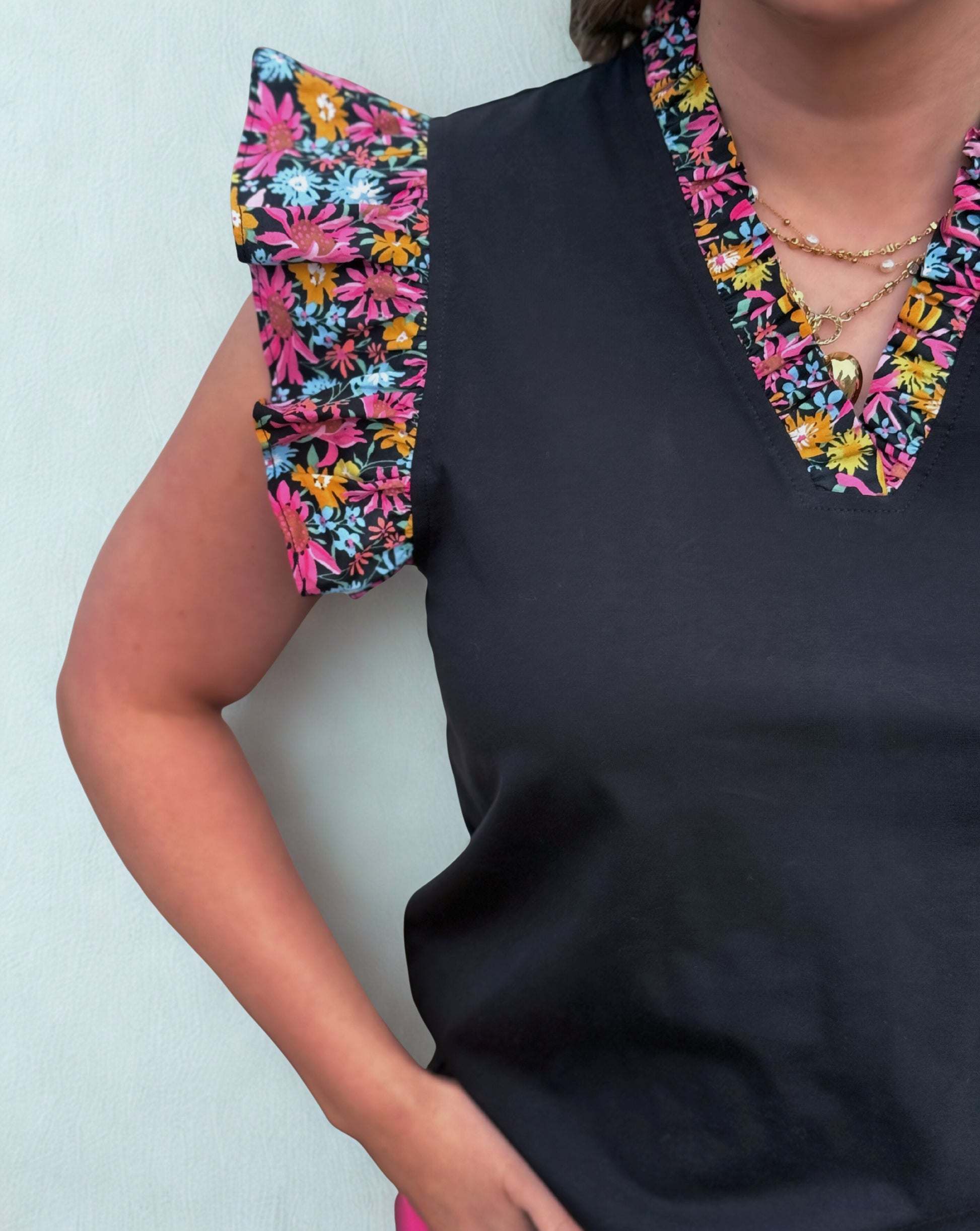 Black top with colorful floral shoulder pads against a light background