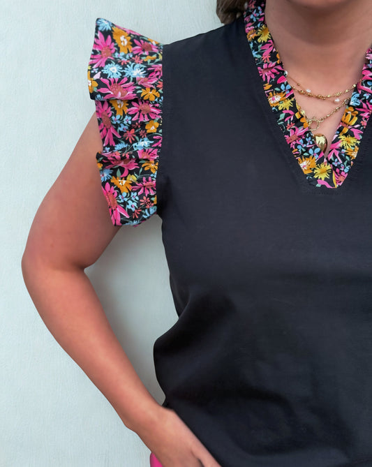Black top with colorful floral shoulder pads against a light background