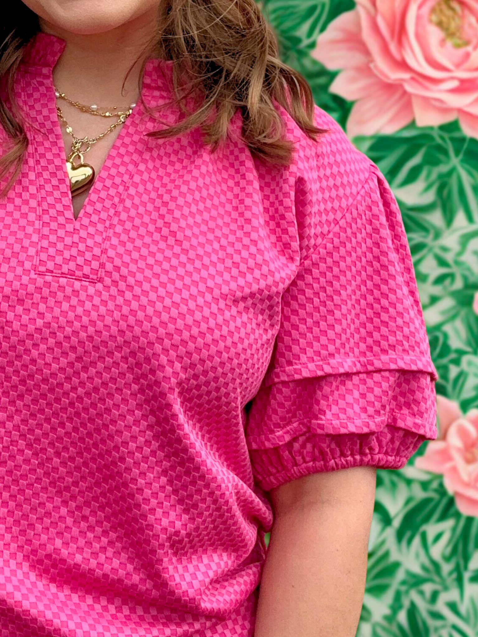 Person wearing a pink blouse with ruffled sleeves against a floral background