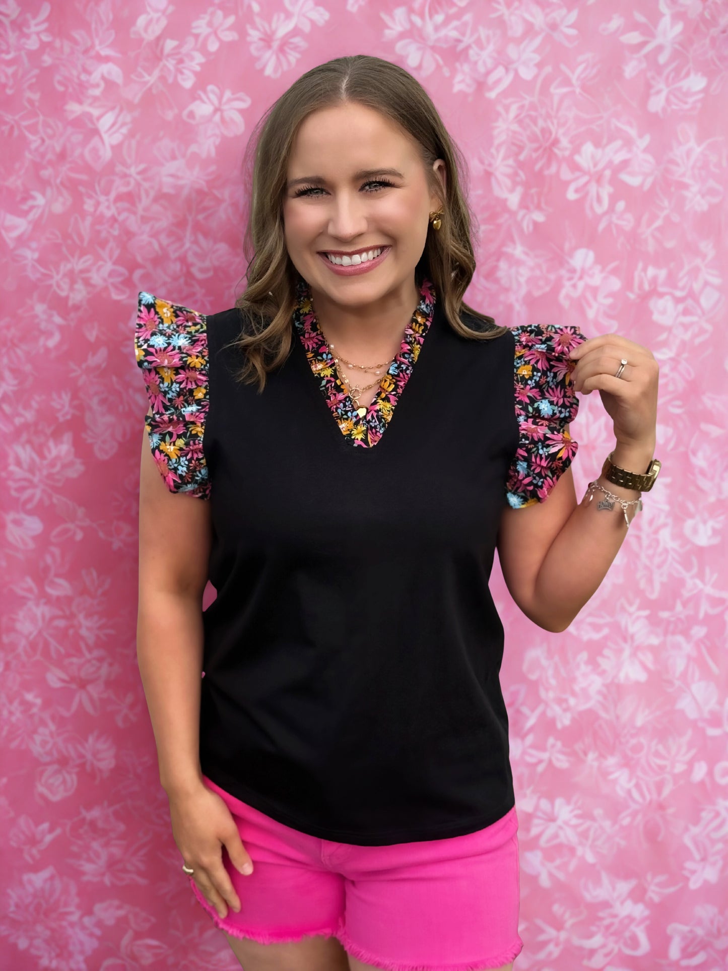 Woman wearing a black top with colorful sleeves and pink shorts against a pink floral background