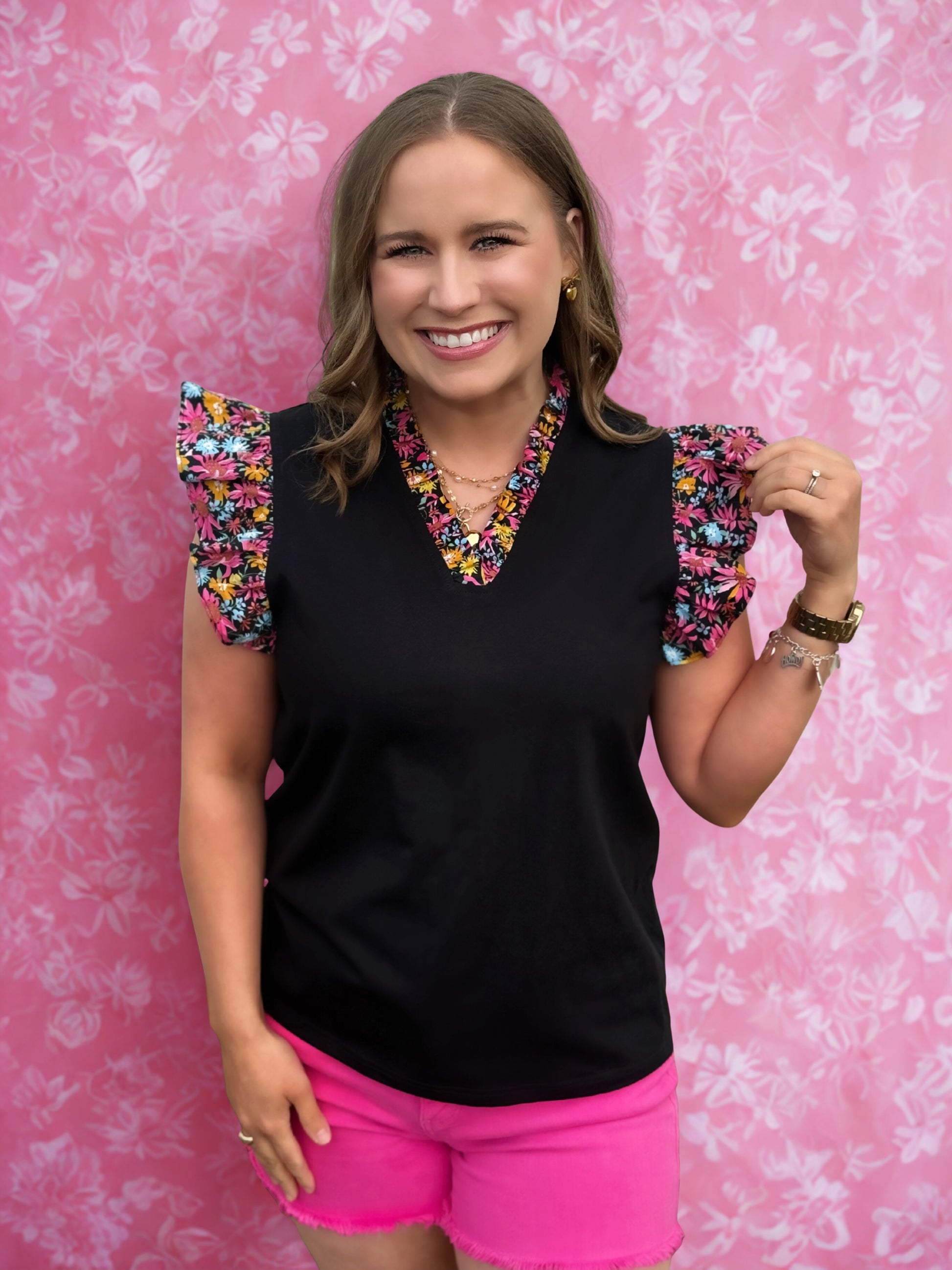 Woman wearing a black top with colorful sleeves and pink shorts against a pink floral background