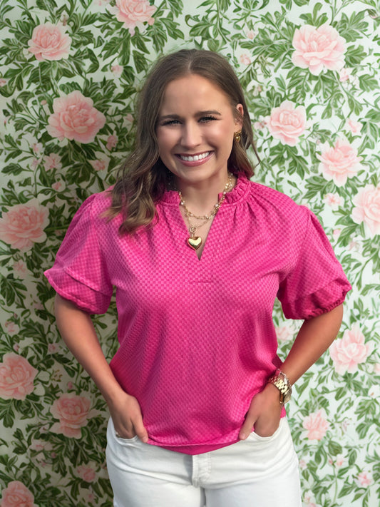 Woman wearing a pink blouse and white pants standing against a floral wallpaper background